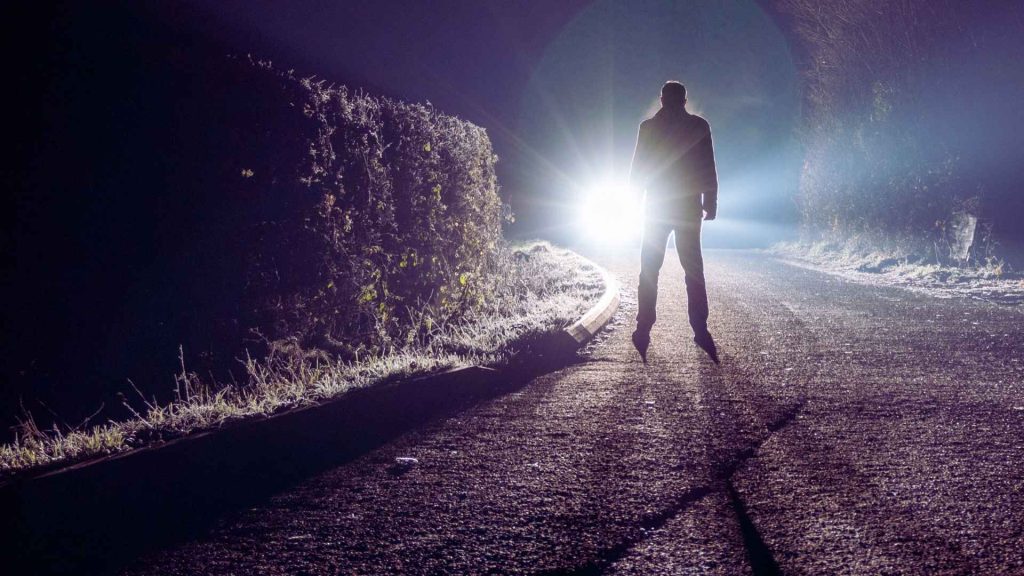 Silhouette facing bright headlights at night, representing risk and uncertainty linked to fentanyl exposure.