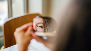 Bipolar 1 vs. Bipolar 2 hero image of a woman looking in a mirror.